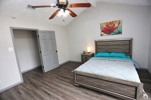 A bedroom with a bed, a ceiling fan, a nightstand, and a door. - Modern Spacious Home in Quiet Neighborhood (La Porte)