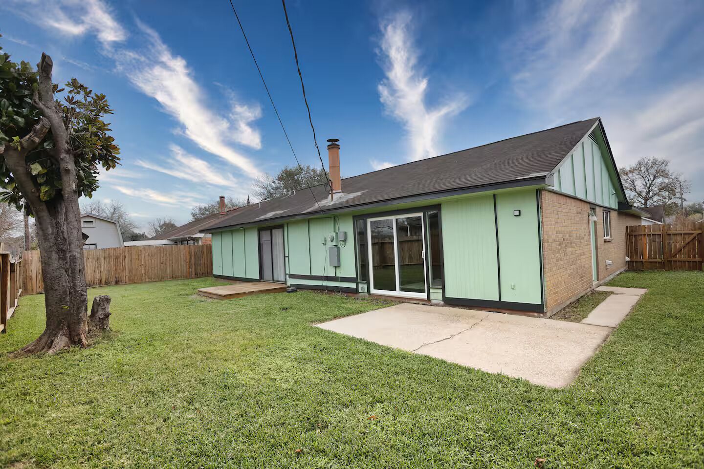 A single-story house with a green exterior, a chimney, a covered patio, and a fenced backyard. - Modern Spacious Home in Quiet Neighborhood (La Porte)