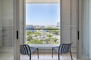 Ein Balkon mit zwei Stühlen und einem Tisch, mit Blick auf eine Stadtlandschaft aus Gebäuden und Grünflächen.