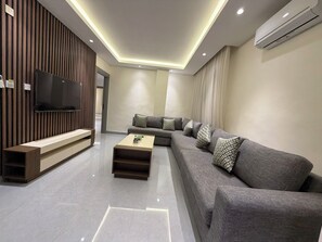 Una sala de estar moderna con un sofá modular, una mesa de centro, un televisor de pantalla plana montado en un panel de madera e iluminación empotrada en el techo.