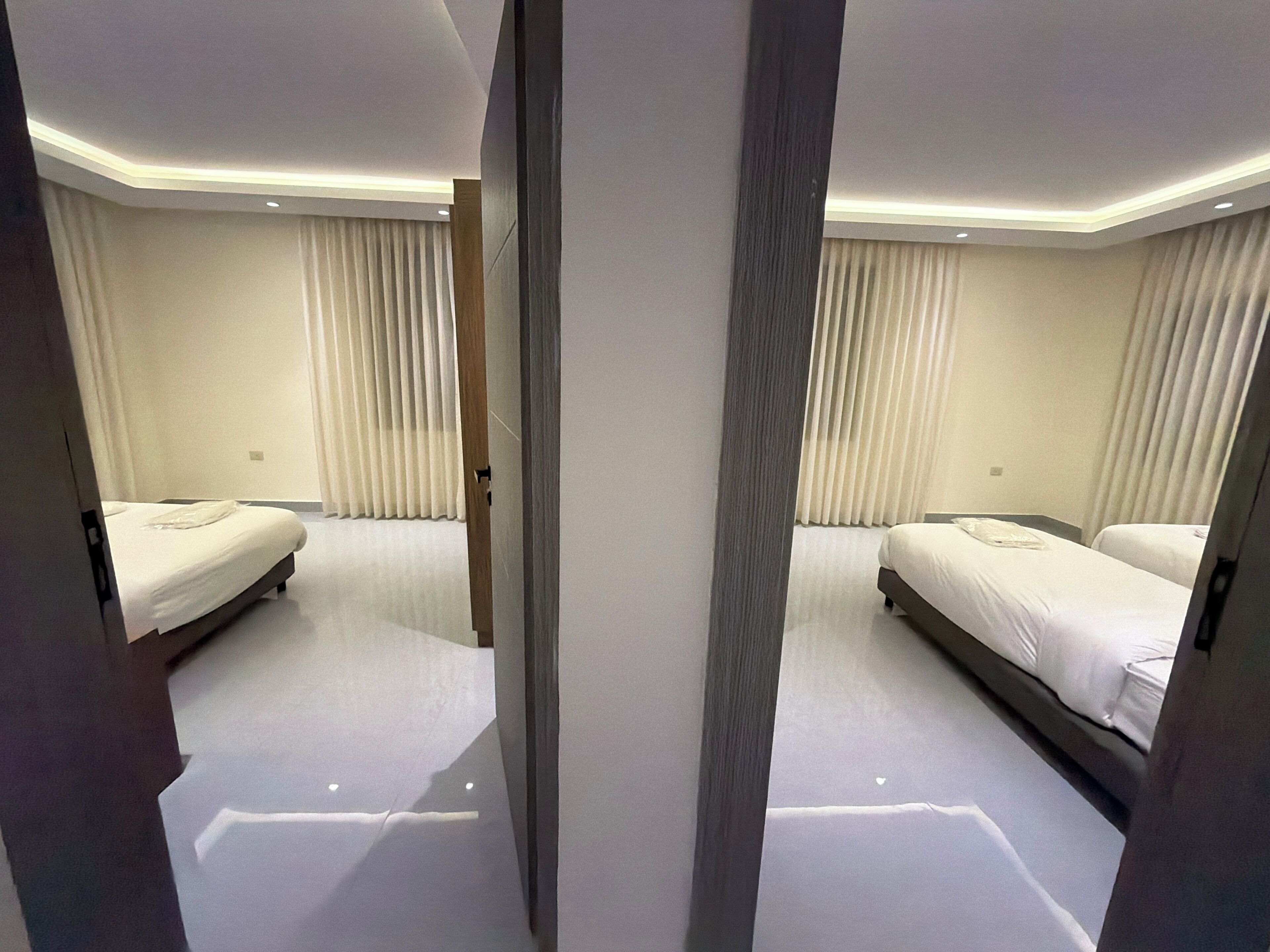 Ein Hotelzimmer mit zwei Betten, einem großen Fenster mit Vorhängen und einem modernen Deckenbau.