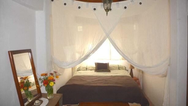 A bedroom with a canopy bed, a bedside table with a mirror and flowers, and a hanging light fixture. - Arco Iris Farm surrounded by mountains and nature in the Sacred Valley Vilcabamba (Vilcabamba)