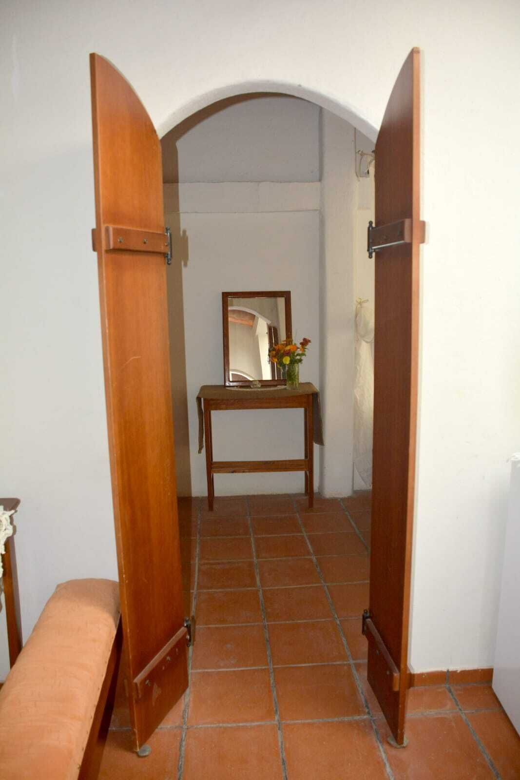 A hallway with a wooden door, a tiled floor, a small table with a mirror and flowers, and a bench.