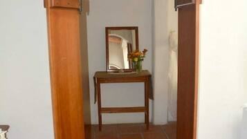 A hallway with a wooden door, a tiled floor, a small table with a mirror and flowers, and a bench.