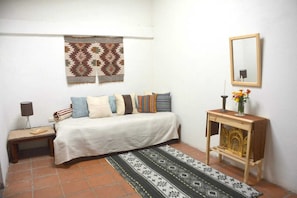 A bedroom with a bed, bedside table, lamp, mirror, and a decorative rug.