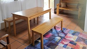 A room with a wooden dining table, a bench, a colorful rug, a wooden bench with cushions, a coat rack, and a door leading outside. - Arco Iris Farm surrounded by mountains and nature in the Sacred Valley Vilcabamba (Vilcabamba)