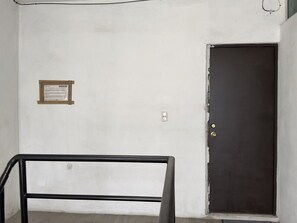 Een kamer met een witte muur, een donkere deur, een klein plaquette en een metalen leuning.