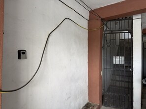 Une façade d’immeuble avec une grille métallique, une boîte électrique fixée au mur et un câble apparent.