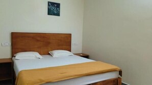 A single bed with a wooden headboard, two white pillows, a brown blanket, and a small bedside table with a lamp. - Laya Crest (Chennai)