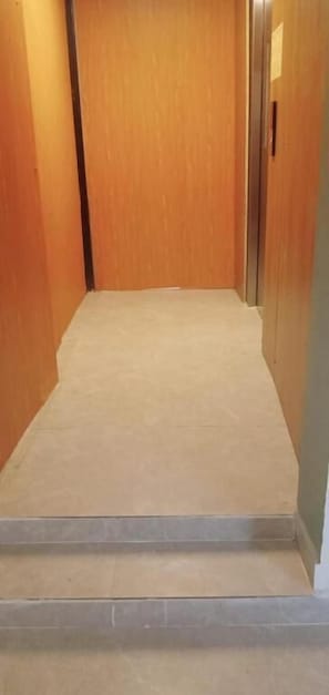A narrow hallway with a wooden door at the end and a small set of steps leading up to it. - Laya Crest (Chennai)