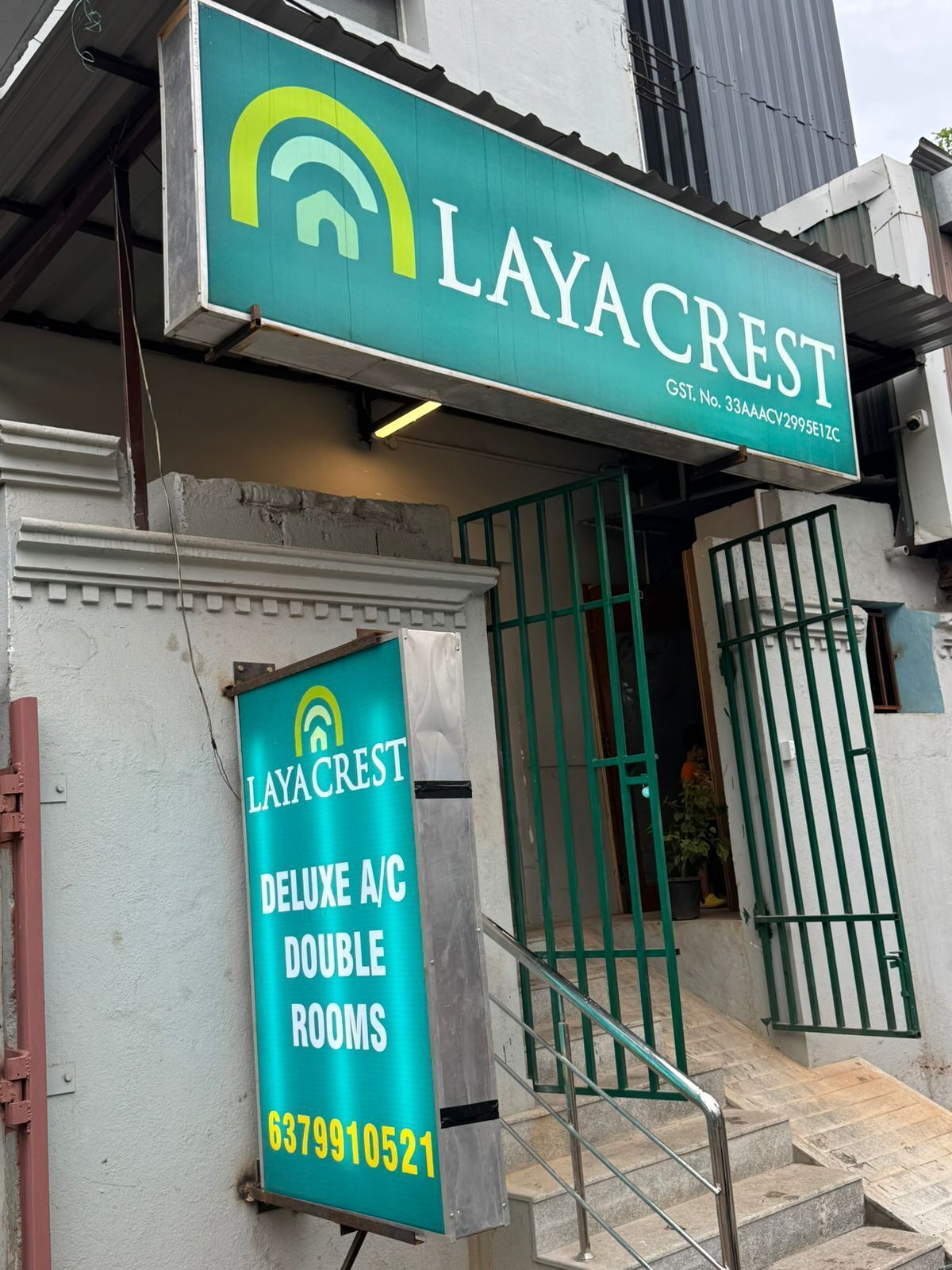 Un edificio con un cartello per camere doppie Layacrest Deluxe con aria condizionata, un ingresso con cancello e una scala che conduce all'ingresso.