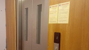 A wooden elevator door with a control panel and two vertical windows. - Laya Crest (Chennai)