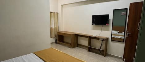 Quarto de hotel com cama, escrivaninha, televisão e armário.