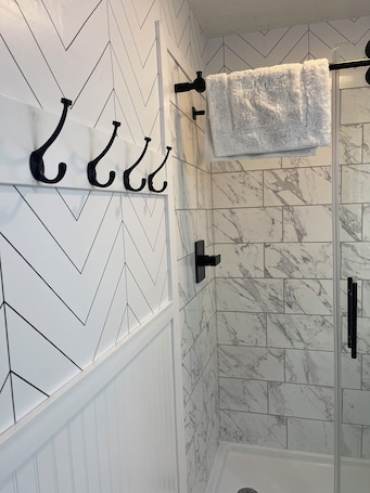 A bathroom with a white and black chevron-patterned wall, a marble-tiled shower area, and a towel rack with a fluffy white towel.. Tranquil 2-bedroom apartment with AC in charming Cambridge/Jeffersonville