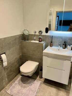 A bathroom with a toilet, sink, mirror, and towel rack. - Bright two-room space in the center (Würzburg)