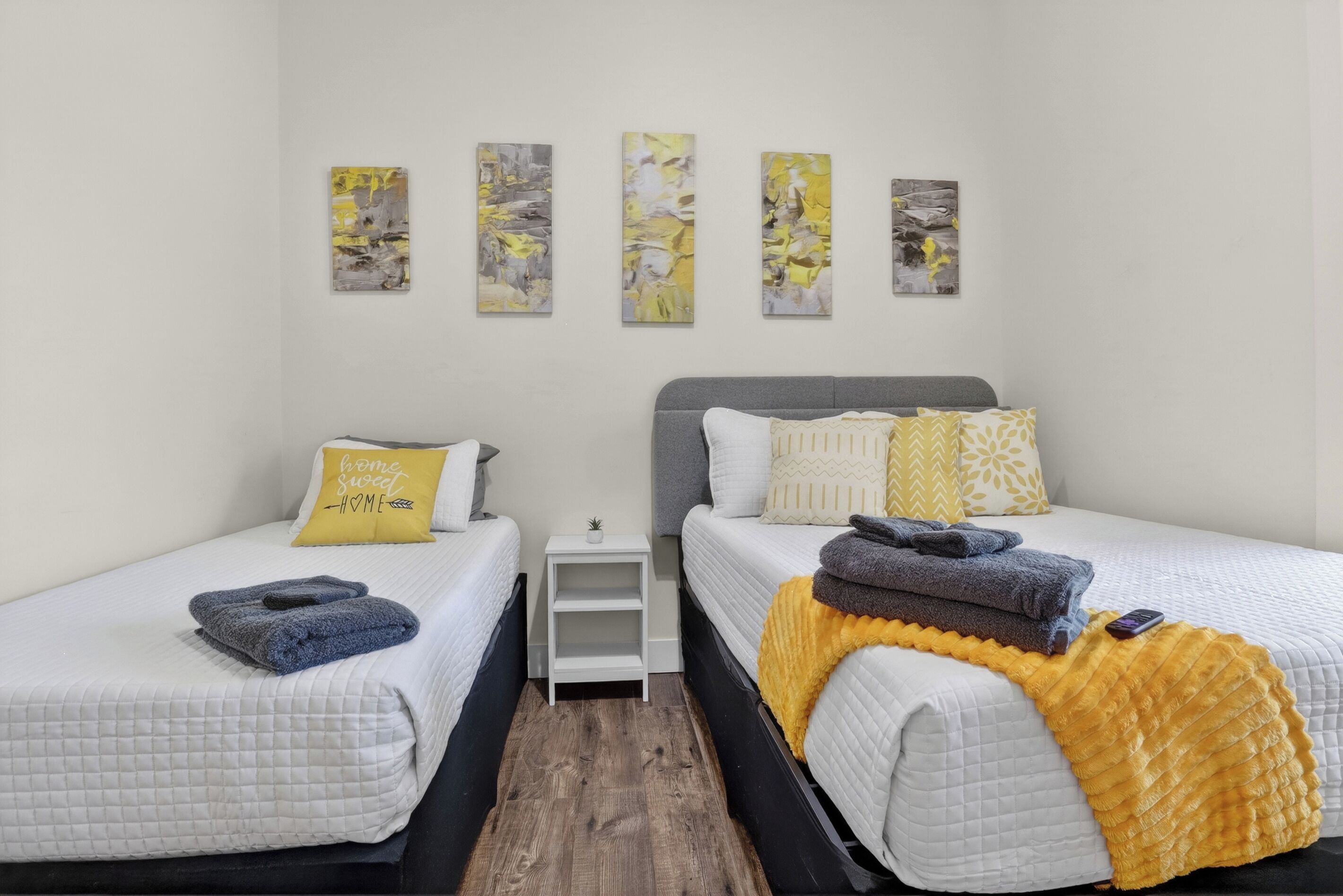 Habitación de hotel con dos camas, una mesita de noche pequeña y cuatro obras de arte colgadas en la pared.