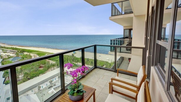 Een balkon met uitzicht op strand en zee, een potorkidee en een houten stoel.