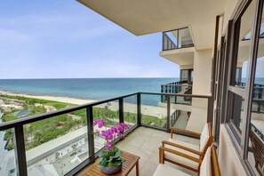 A balcony with a view of the beach and ocean, a potted orchid, and a wooden chair. - Gorgeous Ocean View Beachfront Resort Condo | 1604 (Miami Beach)