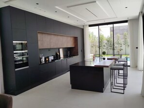 A modern kitchen with a central island, dark cabinetry, and a large window offering a view of the outdoors. - Modern villa at the new Amelkis Golf Resort Marrakech (Marrakech)