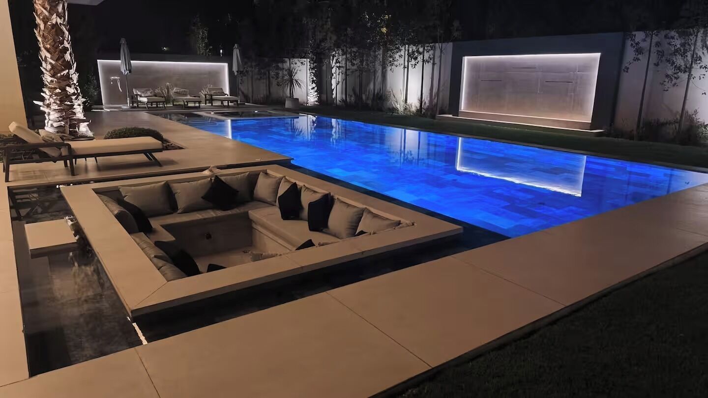 Un espace piscine extérieur moderne, doté de chaises longues et d’un coin salon.