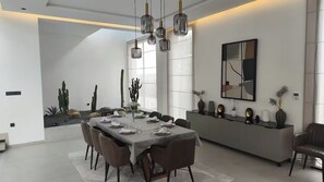 A modern dining room with a long table set for six, surrounded by chairs. There is a decorative cactus arrangement on the left, a large abstract painting on the wall, and a sleek console table with decorative items on the right. - Modern villa at the new Amelkis Golf Resort Marrakech (Marrakech)