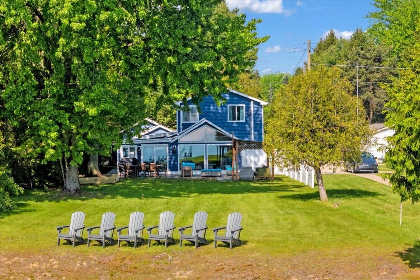 Une maison dotée d’un patio couvert, d’un espace salon extérieur et d’une pelouse agrémentée de fauteuils Adirondack.