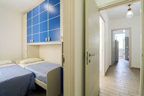 Ein Schlafzimmer mit zwei Betten, einem Kleiderschrank mit blauen Paneelen und einem Flur, der zu einem Badezimmer führt.
