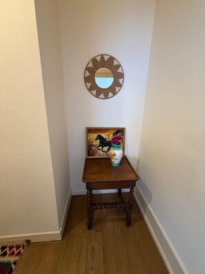 A corner with a wooden table, a vase with flowers, a framed picture, and a woven mirror on the wall. - Apartment with breathtaking view of the vineyard and quiet village center (Montréal)