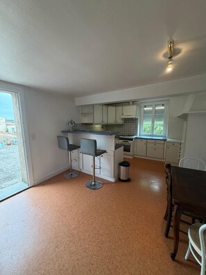 A kitchen with a central island, two bar stools, a dining table with chairs, and a trash can. - Apartment with breathtaking view of the vineyard and quiet village center (Montréal)