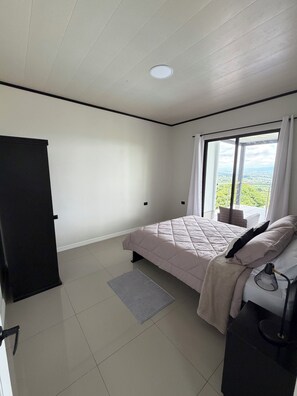 Une chambre à coucher avec un lit, une fenêtre donnant sur un paysage agréable, une porte et un luminaire au plafond.