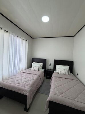 Une chambre avec deux lits, une table de chevet, une lampe et une fenêtre avec des rideaux.