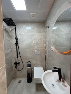 Un baño moderno con ducha, inodoro y lavamanos, con paredes de mármol y tragaluz.