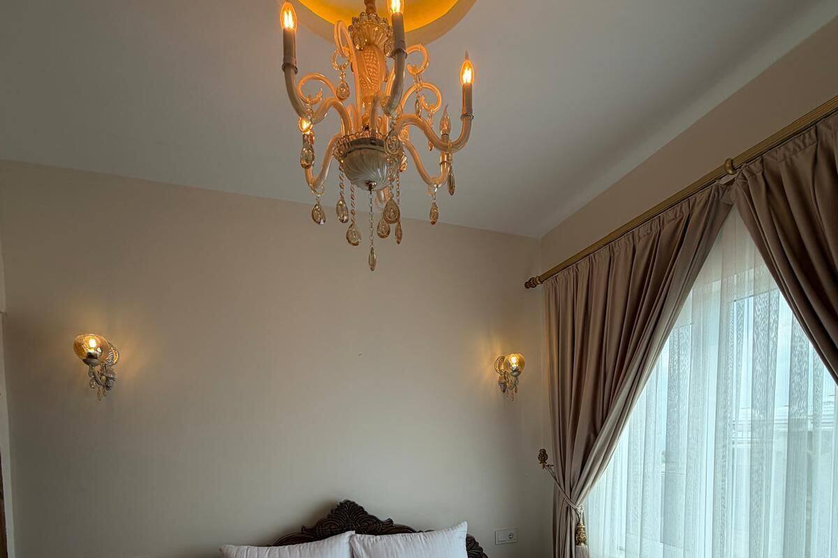 A hotel room with a large bed, a chandelier, and curtains on a window.