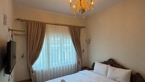Habitación de hotel con una cama grande, un candelabro, un televisor y una ventana con cortinas.