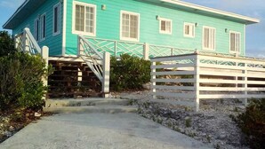 A turquoise building with a white fence, a concrete pathway, and some greenery. - Anchorage - 4BR Luxury Beach House in Exuma – 50ft to calm water, Sleeps 10 (Black Point)