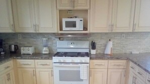 A kitchen with light-colored cabinets, a white stove, a microwave, and a tiled floor. - Anchorage - 4BR Luxury Beach House in Exuma – 50ft to calm water, Sleeps 10 (Black Point)
