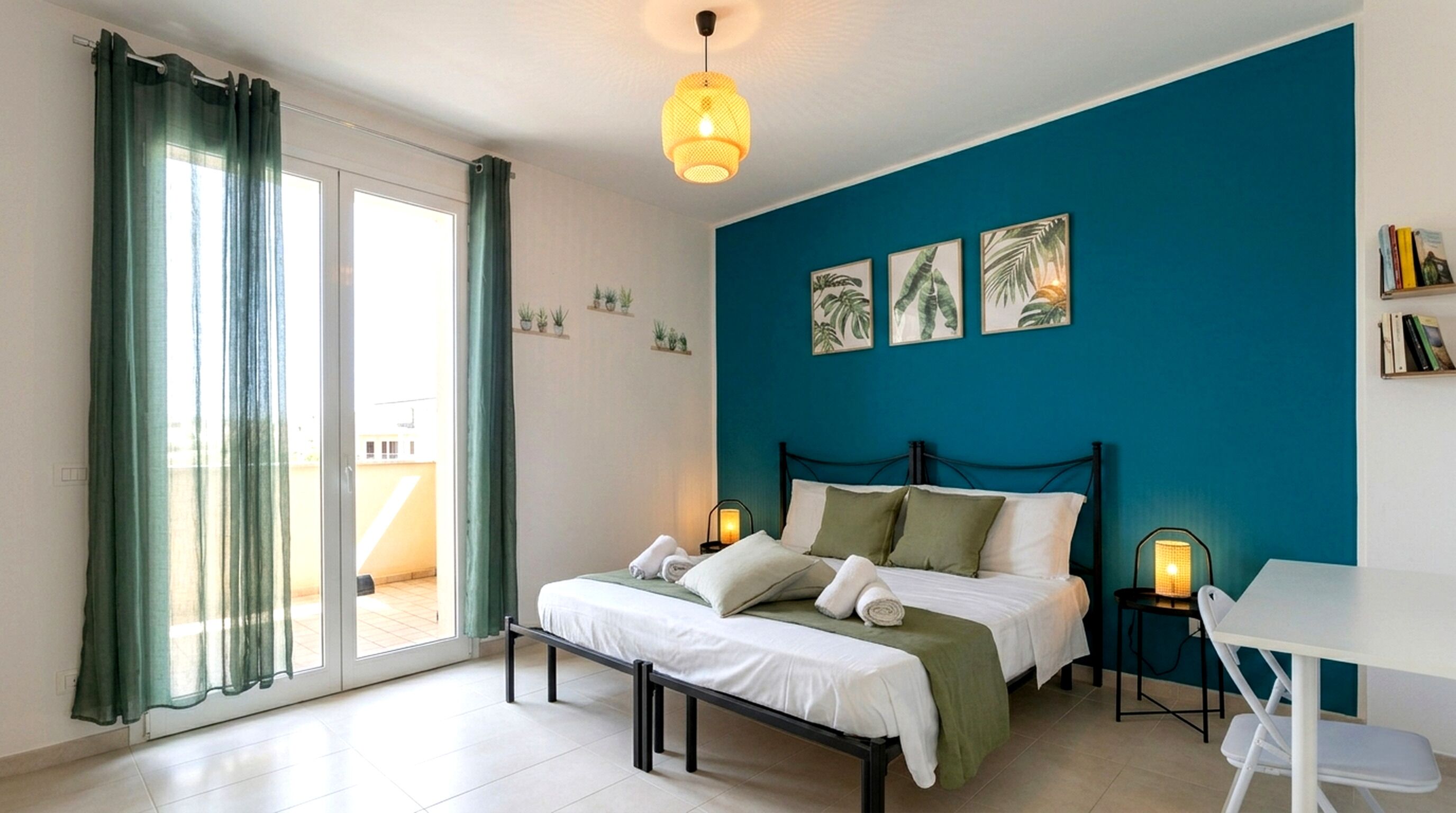 A bedroom with a bed, bedside tables, a desk, and a view of the outside.