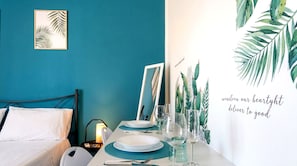 A neatly arranged dining table with plates, glasses, and a candle, set against a teal wall with a cactus plant and a framed artwork. - Concy's Jacuzzi - Private Suite with Sea View and Exclusive Terrace (Kaukana)