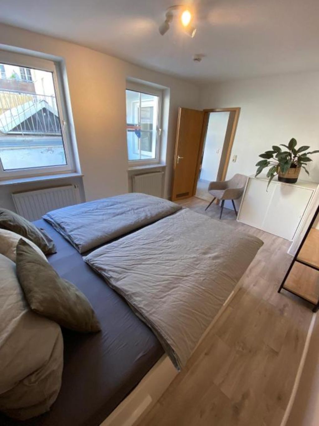 A bedroom with a bed, a chair, a potted plant, and a window.