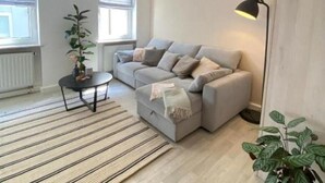 Un salon moderne avec un canapé gris, une petite table ronde, un lampadaire et une plante en pot.