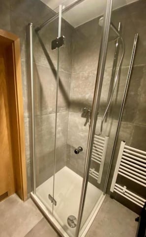 Eine gläserne Duschkabine mit weißem Boden, einem Handtuchhalter und einem an der Wand montierten Heizkörper.
