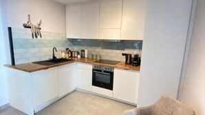 Une cuisine moderne avec des meubles blancs, un plan de travail en bois, un four encastré et une chaise.