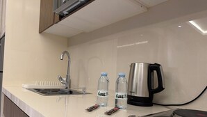Eine Küche mit Spüle aus Edelstahl, Wasserkocher und zwei Wasserflaschen auf der Arbeitsplatte.