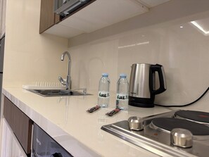 A kitchen with a stainless steel sink, a kettle, and two water bottles on the counter. - 302 JRE Rooftop With Stunning Boulevard Veiw (Amman)