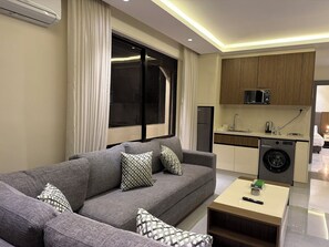 A modern living room with a grey sofa, patterned cushions, a coffee table, and a built-in washing machine. - 302 JRE Rooftop With Stunning Boulevard Veiw (Amman)
