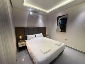 Quarto de hotel moderno com uma cama grande, mesas de cabeceira, aparelho de ar condicionado e um quadro na parede.