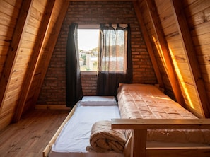 A small, cozy attic bedroom with a wooden sloped ceiling, a single bed, and a window with curtains.