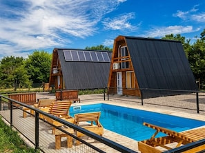 A modern house with a swimming pool, solar panels, and wooden deck furniture.
