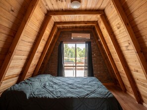 A room with a sloped ceiling, a bed, a window, and a thermostat.