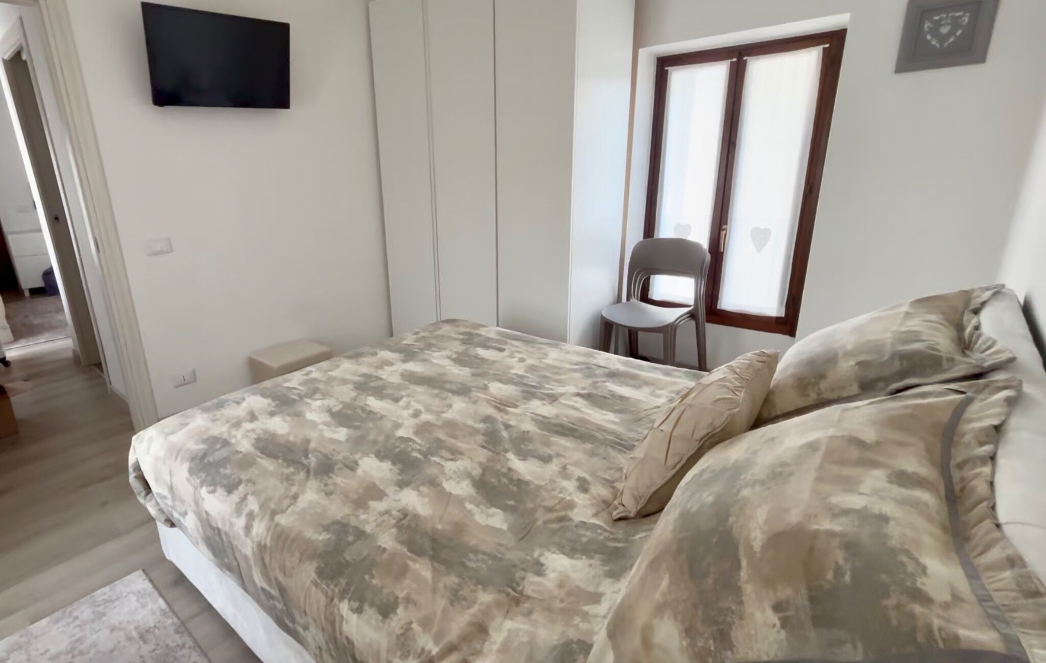 A bedroom with a bed, a chair, a TV, and a window.
